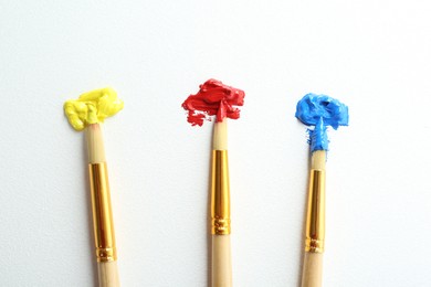 Brushes with bright paints on white background, top view