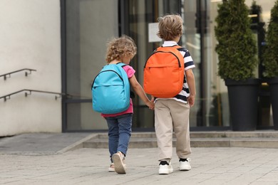 Photo of Brother and sister walking to kindergarten outdoors, back view