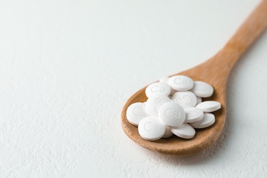 Photo of Calcium supplement pills in wooden spoon on white table, closeup. Space for text