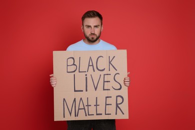 Photo of Young man holding sign with phrase Black Lives Matter on red background. End racism