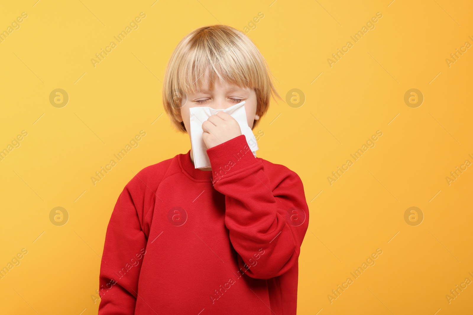 Photo of Boy blowing nose in tissue on orange background, space for text. Cold symptoms