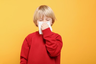 Boy blowing nose in tissue on orange background, space for text. Cold symptoms