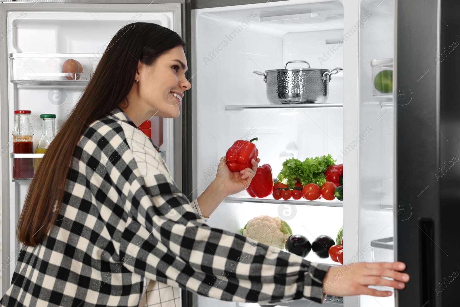 Photo of Young woman taking red bell pepper out of refrigerator