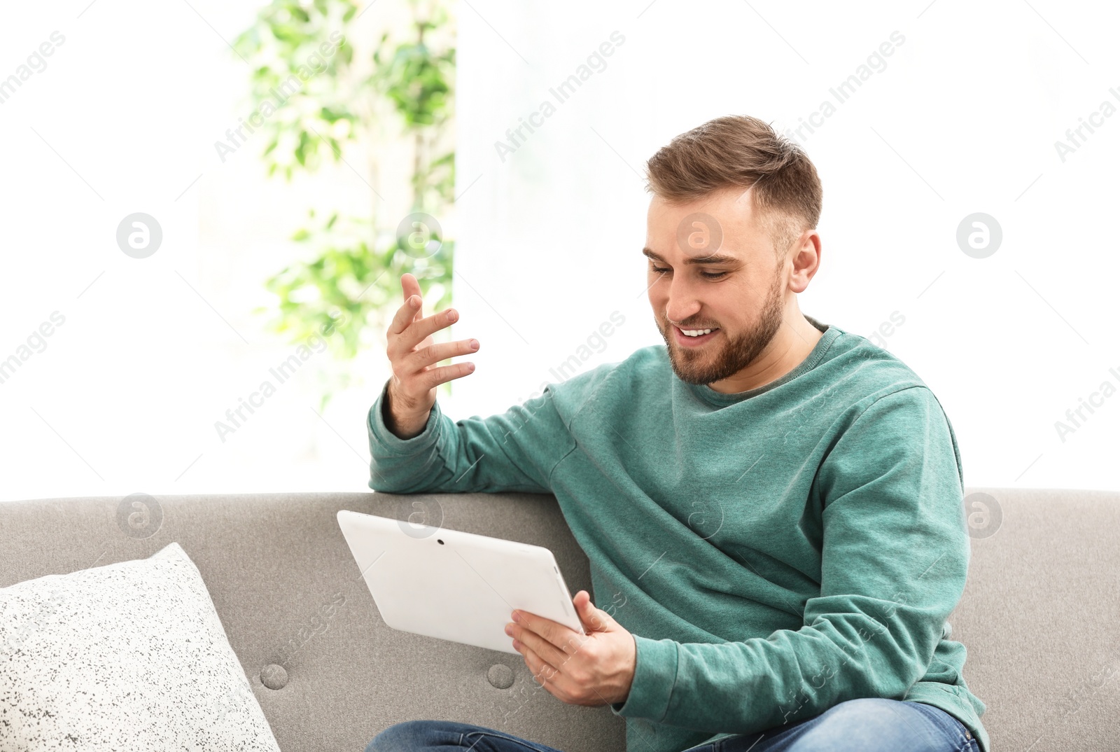 Photo of Young man using video chat on tablet in living room