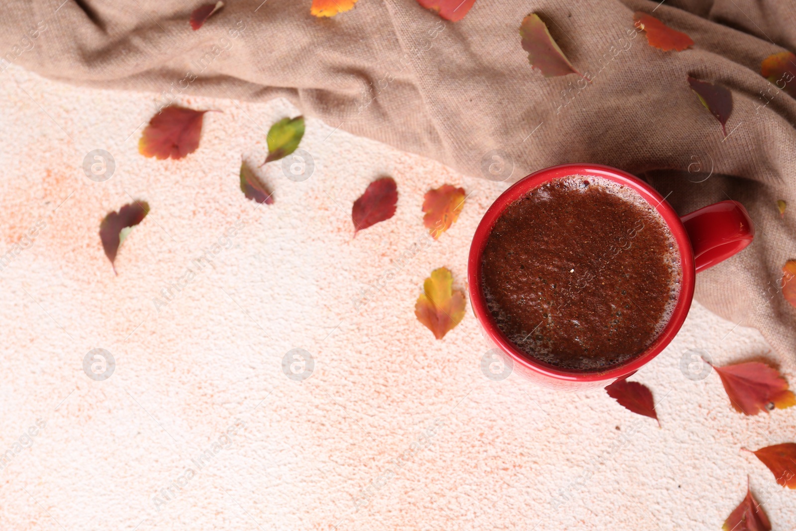 Photo of Cup of hot drink, leaves and soft knitted fabric on beige textured table, flat lay with space for text. Cozy autumn atmosphere