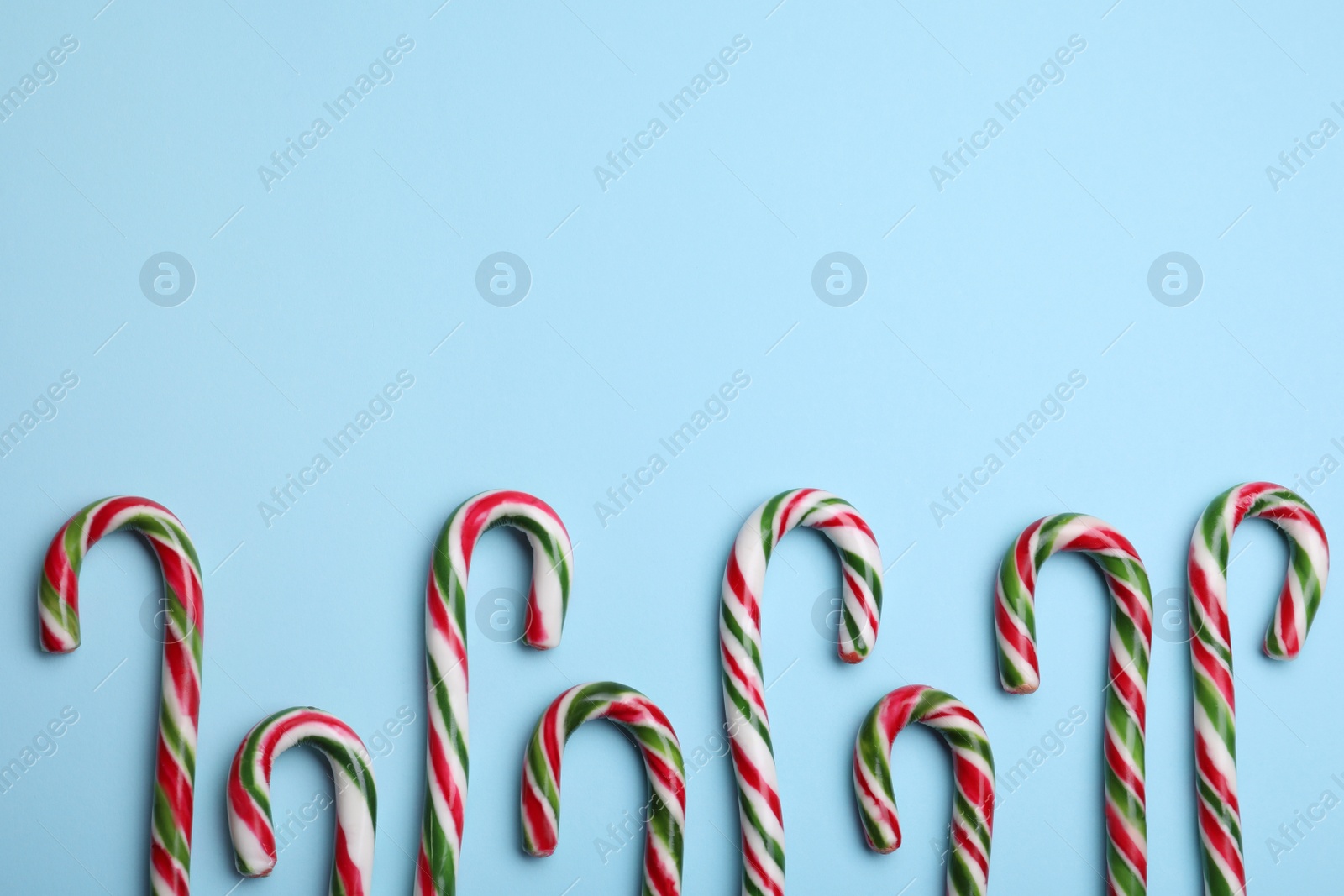 Photo of Many sweet Christmas candy canes on light blue background, flat lay. Space for text