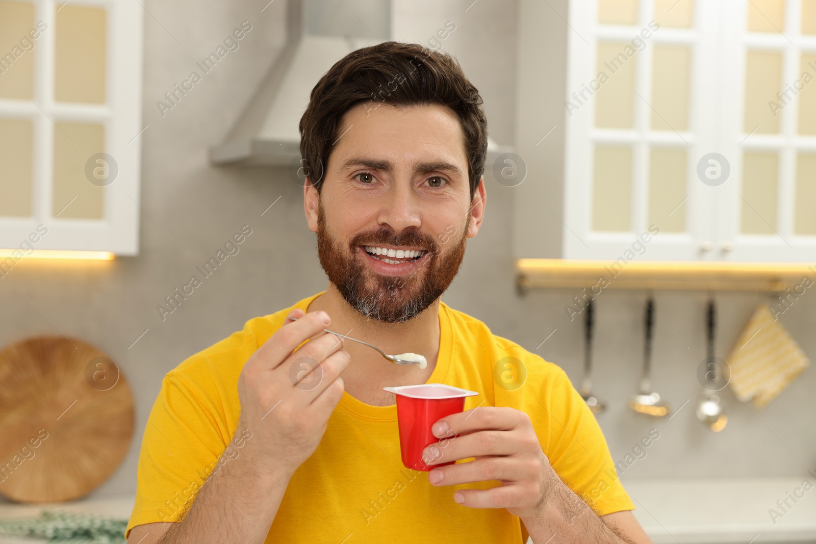 Photo of Handsome man with delicious yogurt in kitchen