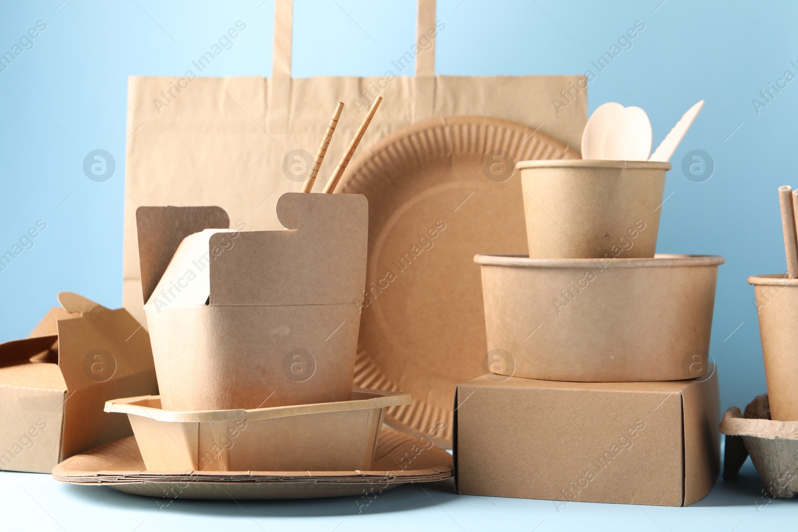 Photo of Eco friendly food packaging. Paper containers, tableware and bag on white table against light blue background