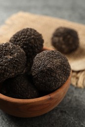 Photo of Black truffles in wooden bowl on grey table, closeup