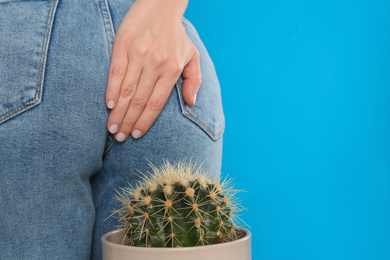 Woman sitting down on cactus against light blue background, space for text. Hemorrhoid concept