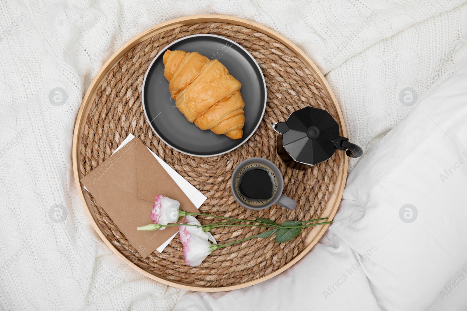 Photo of Tray with tasty croissant, cup of coffee and flowers on white bed, top view