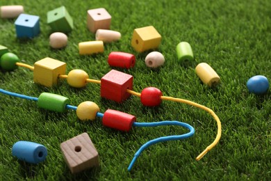 Photo of Wooden pieces and strings for threading activity on artificial grass, closeup. Educational toy for motor skills development