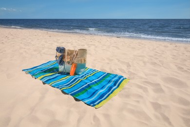 Photo of Striped beach towel and bag with accessories on sandy seashore, space for text