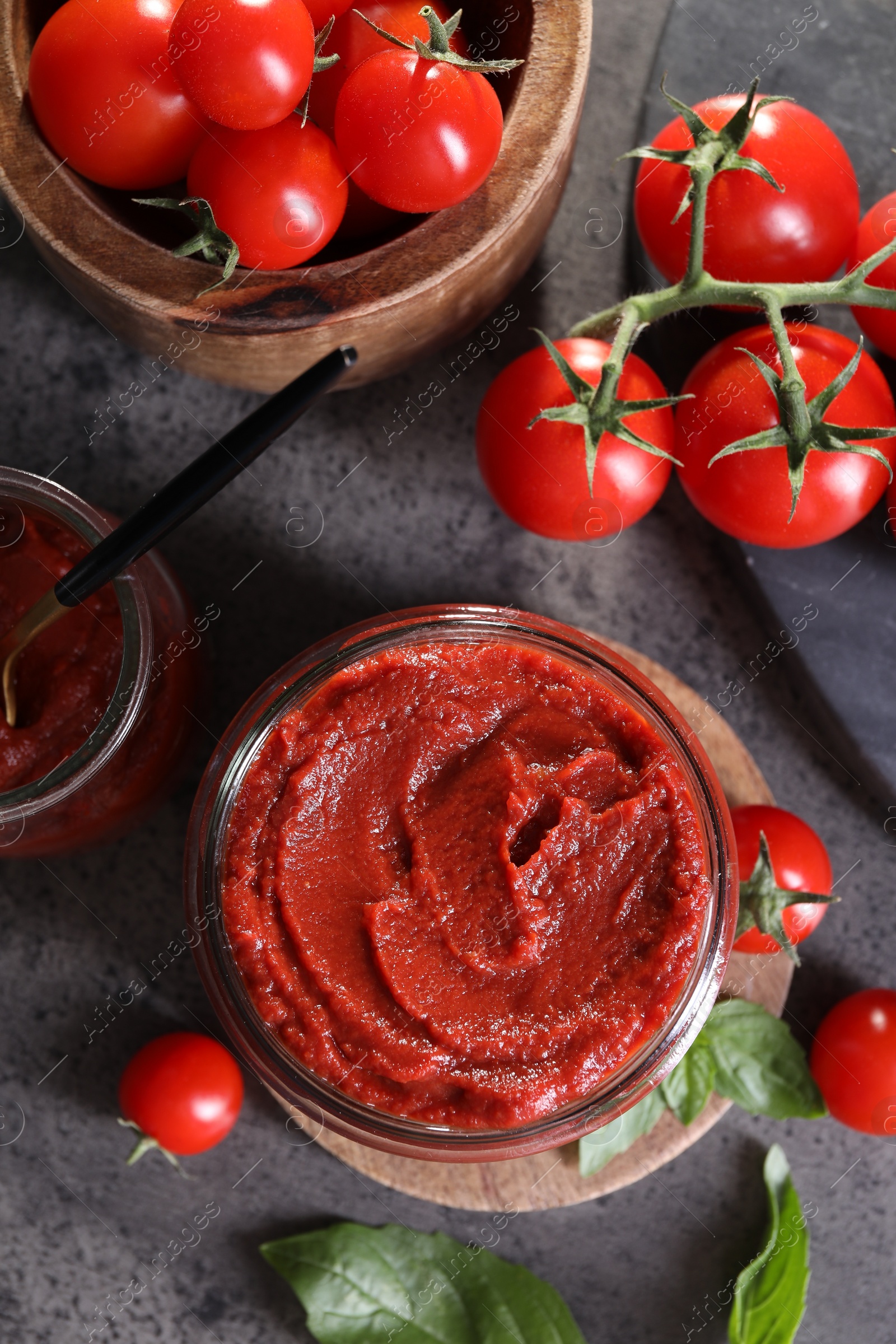 Photo of Jar of tasty tomato paste and ingredients on grey textured table, flat lay