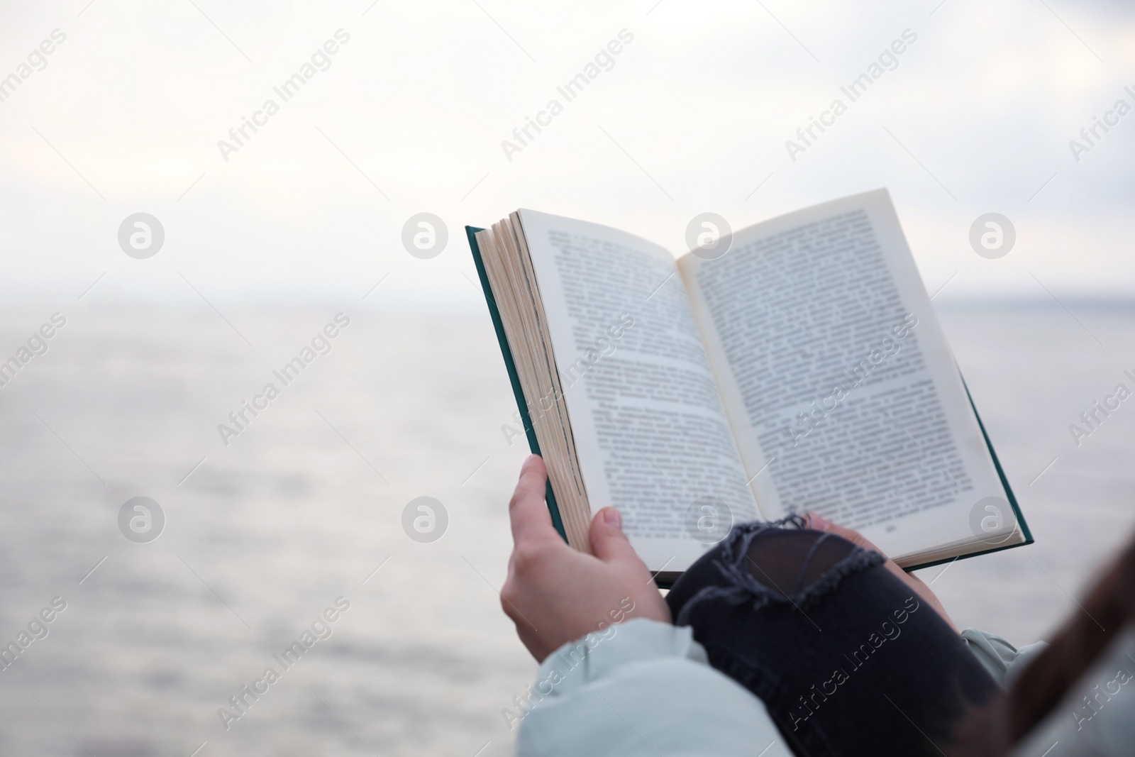 Photo of Woman reading book near river on cloudy day, closeup