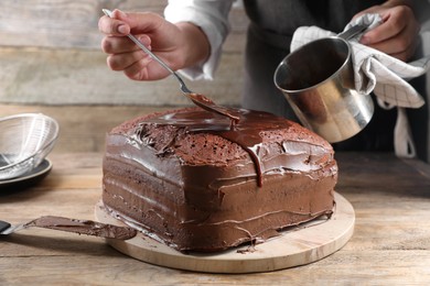 Photo of Woman pouring chocolate cream into homemade sponge cake at wooden table, closeup