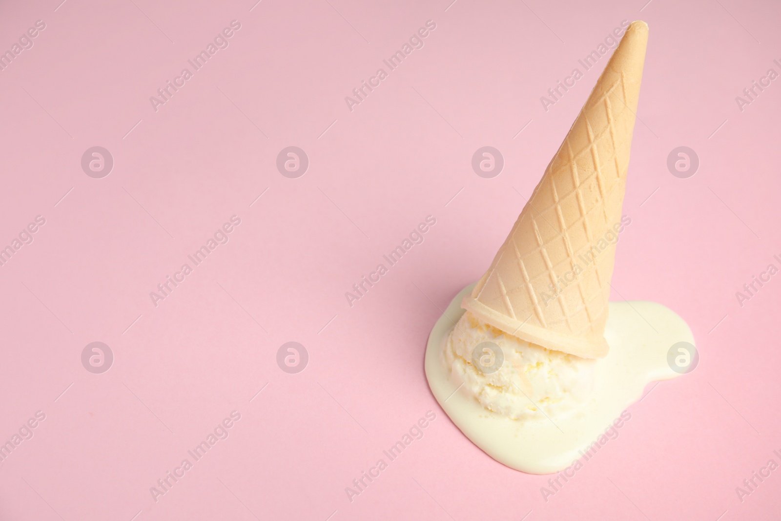 Photo of Melted  vanilla ice cream in wafer cone on pink background. Space for text