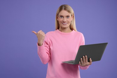 Photo of Special promotion. Smiling woman with laptop pointing at something on purple background