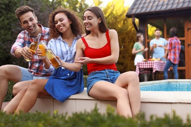 Happy friends with drinks at barbecue party near swimming pool outdoors