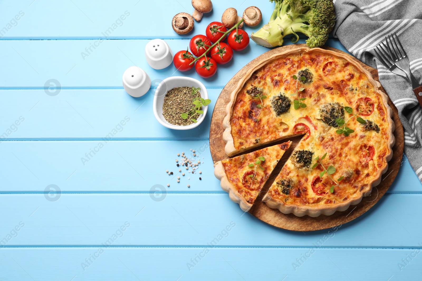 Photo of Delicious homemade vegetable quiche and ingredients on light blue wooden table, flat lay. Space for text