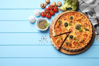 Delicious homemade vegetable quiche and ingredients on light blue wooden table, flat lay. Space for text