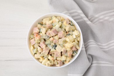 Photo of Tasty Olivier salad with boiled sausage in bowl on white wooden table, top view