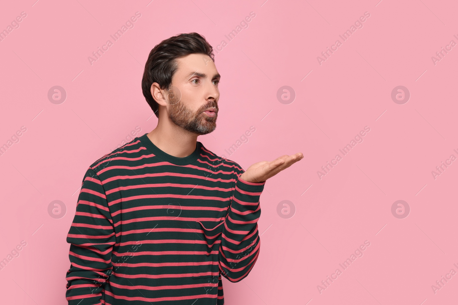 Photo of Handsome man blowing kiss on pink background. Space for text