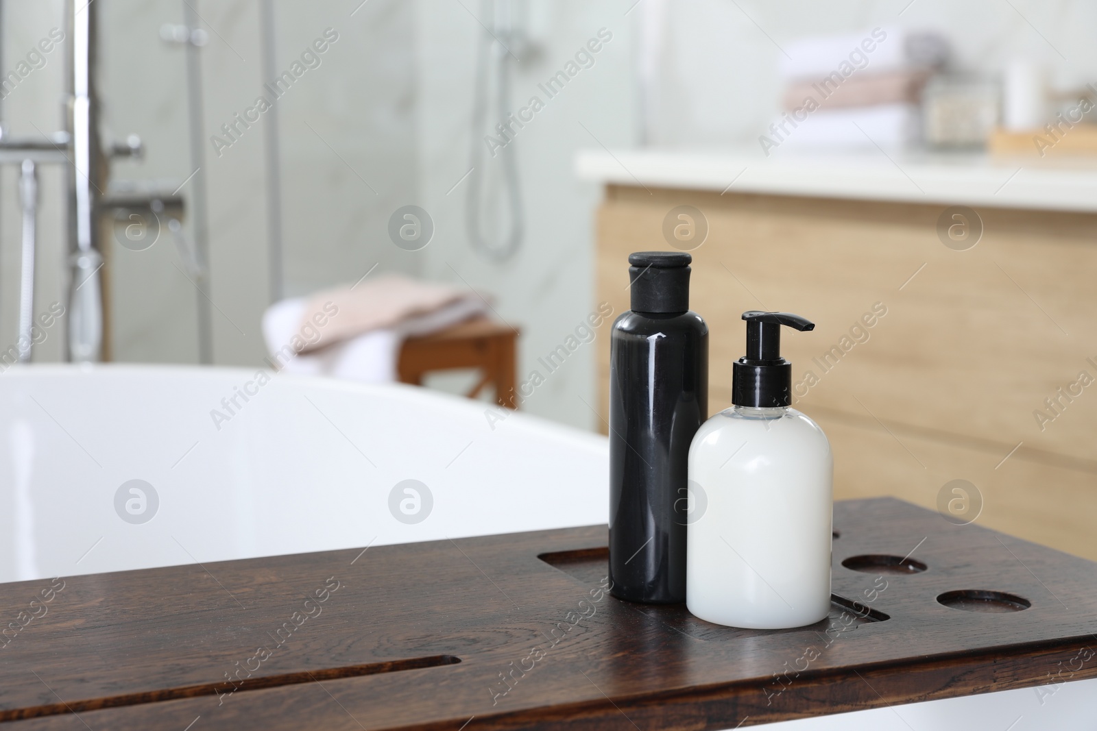 Photo of Wooden bath tray with bottles of shower gels on tub indoors, space for text