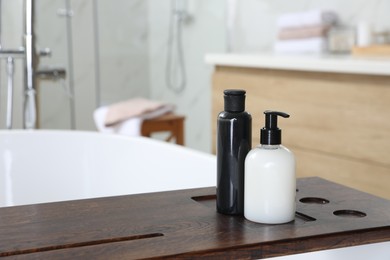 Photo of Wooden bath tray with bottles of shower gels on tub indoors, space for text