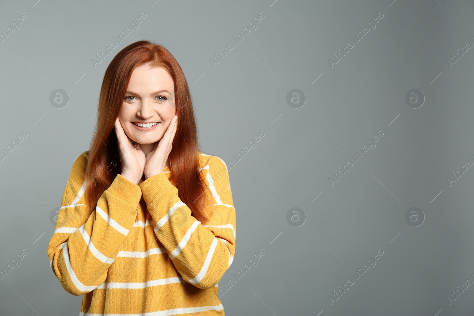 Photo of Candid portrait of happy young woman with charming smile and gorgeous red hair on grey background, space for text