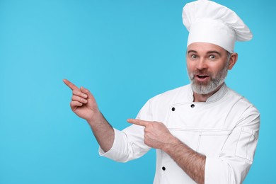 Surprised chef in uniform pointing at something on light blue background