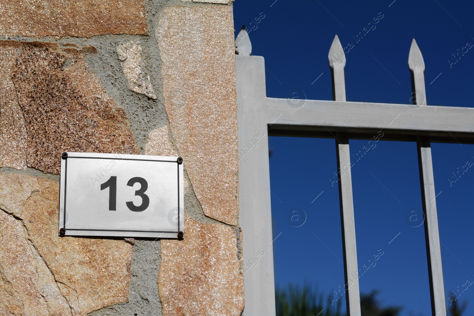 Photo of Plate with number 13 on textured stone wall near metal fence