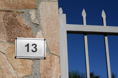 Plate with number 13 on textured stone wall near metal fence