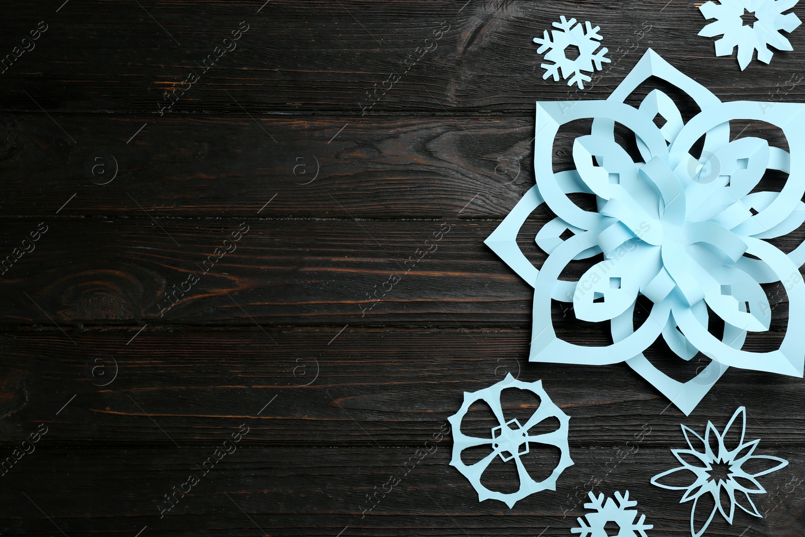 Photo of Light blue paper snowflakes on black wooden table, flat lay. Space for text