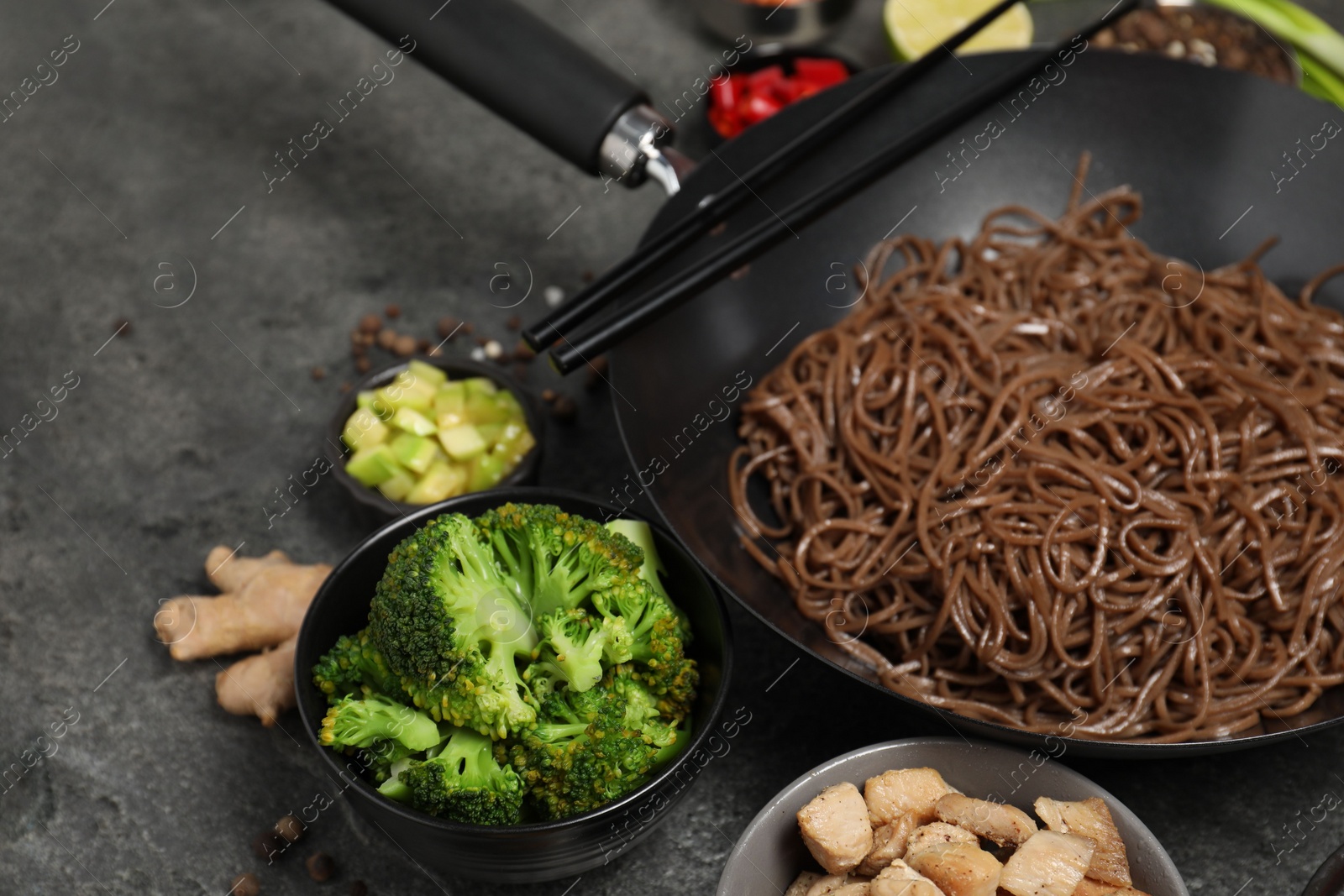 Photo of Wok with noodles, chicken and other products on grey table