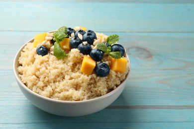 Photo of Tasty quinoa porridge with blueberries, pumpkin and mint in bowl on light blue wooden table, closeup. Space for text