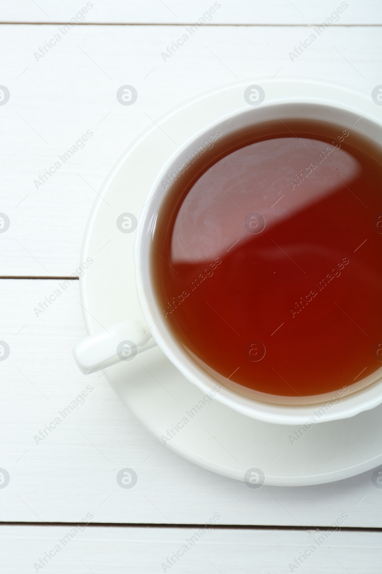 Photo of Aromatic tea in cup on white wooden table, top view