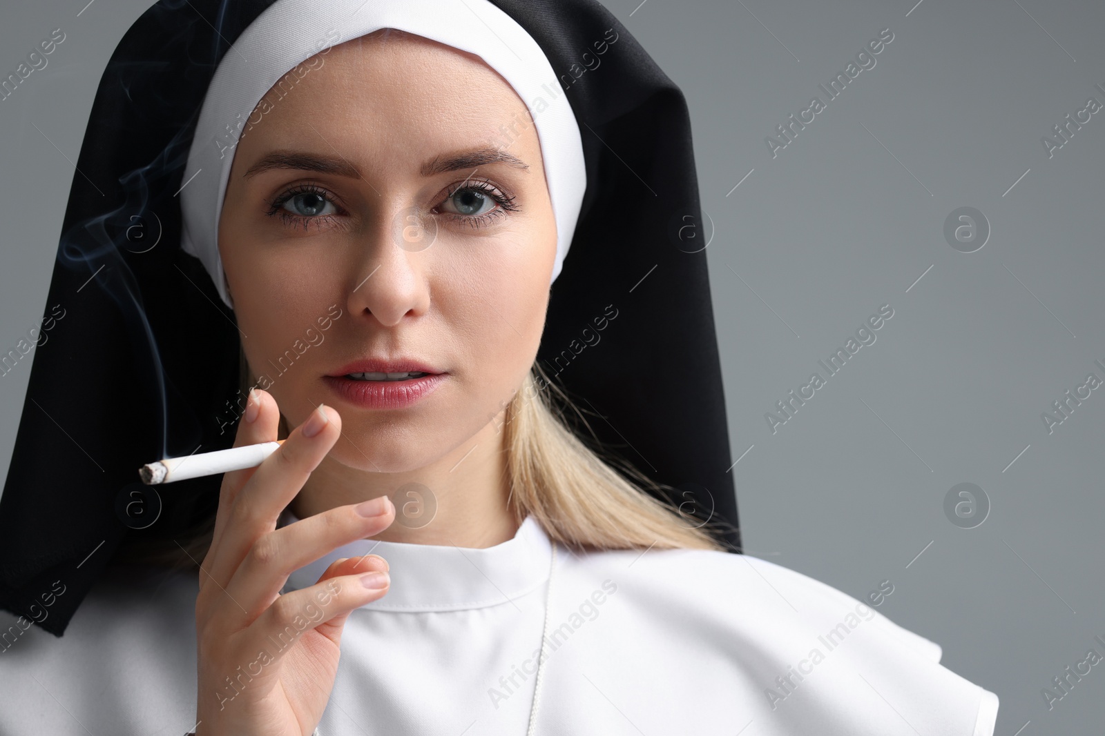 Photo of Woman in nun habit smoking cigarette on grey background. Space for text