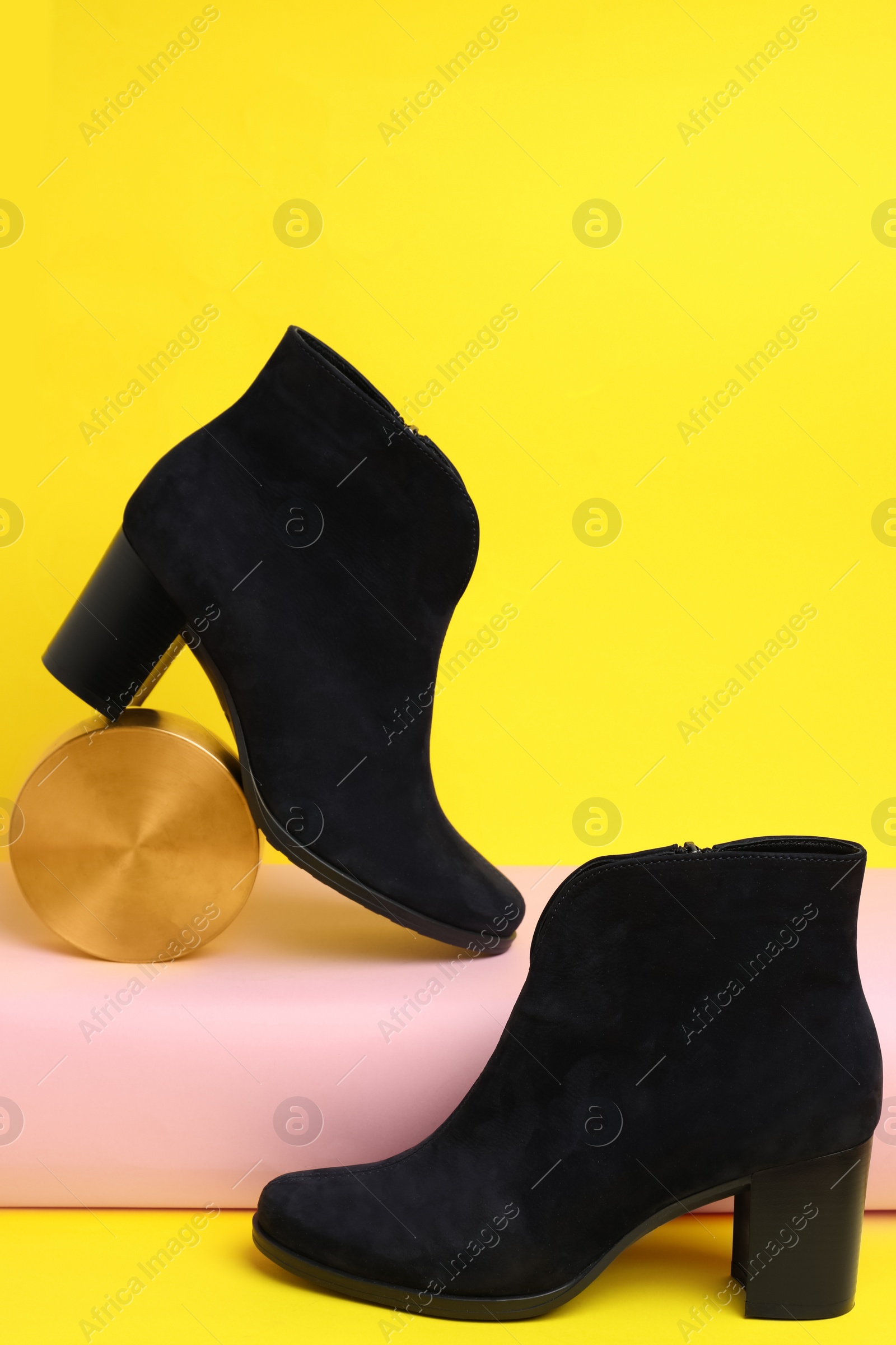 Photo of Stylish black female boots and decor on yellow background