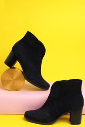 Photo of Stylish black female boots and decor on yellow background