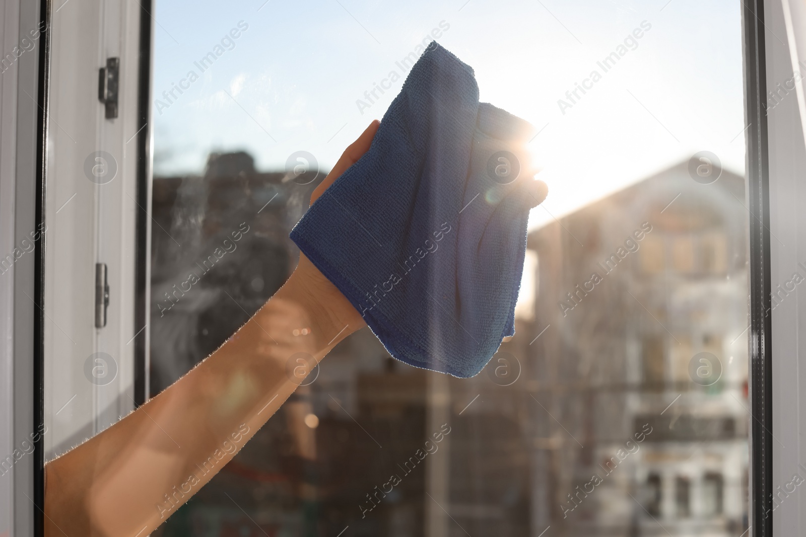 Photo of Young woman cleaning window glass with rag at home, closeup