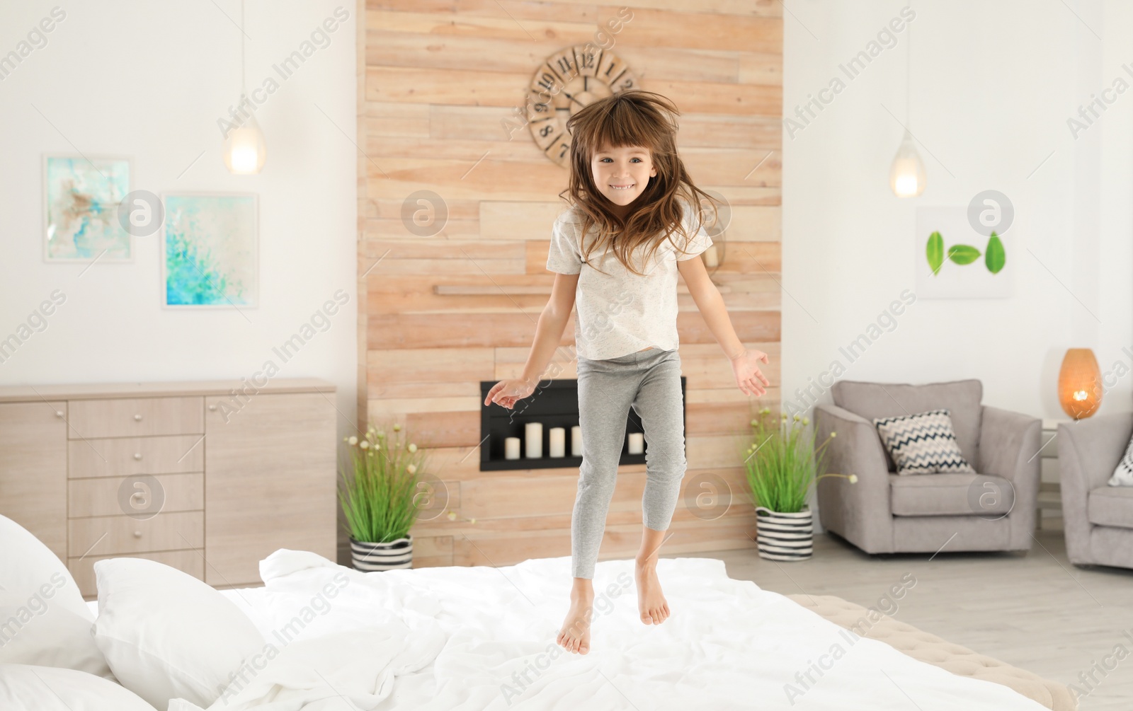 Photo of Cute little girl jumping on bed at home