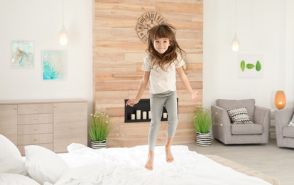 Cute little girl jumping on bed at home