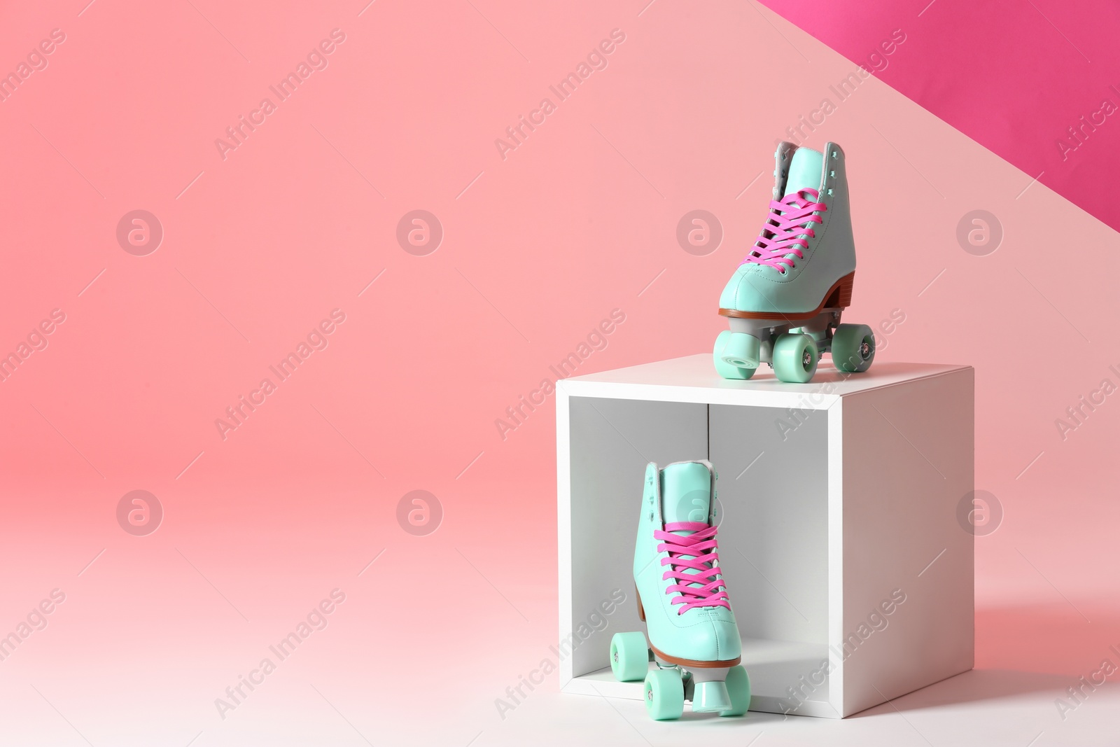 Photo of Pair of vintage roller skates and storage cube on color background. Space for text