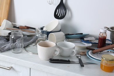 Many dirty utensils and dishware on countertop in messy kitchen