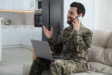 Photo of Happy soldier with laptop talking on phone at home. Military service