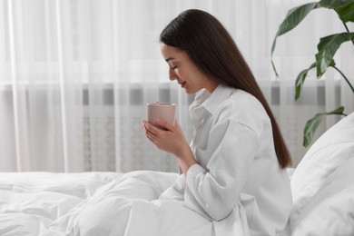 Photo of Smiling woman with cup of drink in bed at home, space for text. Lazy morning
