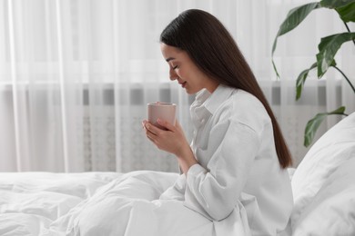 Smiling woman with cup of drink in bed at home, space for text. Lazy morning