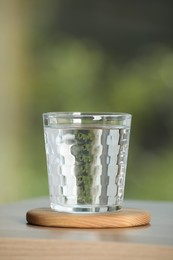 Photo of Glass of pure water on wooden table against blurred green background
