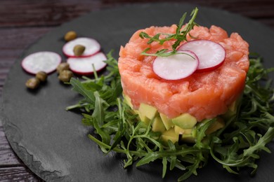 Tasty salmon tartare with radish, avocado and arugula on wooden table, closeup